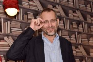 il giornalista Corrado Formigli con gli occhiali da vista e la mano alzata