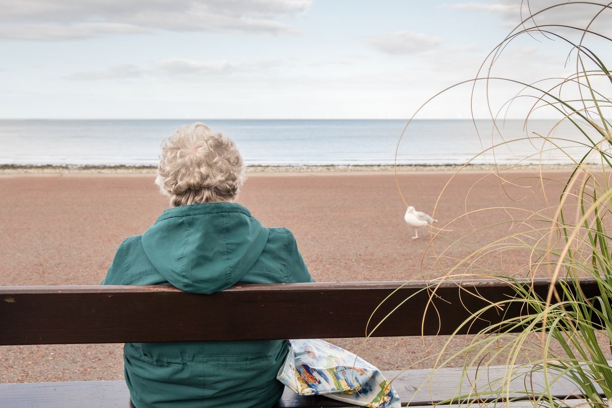 Donna anziana seduta in riva al mare