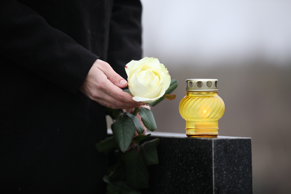 Momento di raccoglimento davanti a una lapide con fiore e cero.