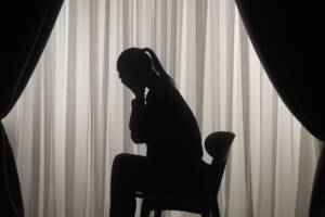 una donna seduta su una sedia che piange nell'ombra