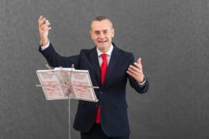 Il giornalista Filippo Poletti ritratto davanti a un leggio in una posa che ricorda un direttore d'orchestra.