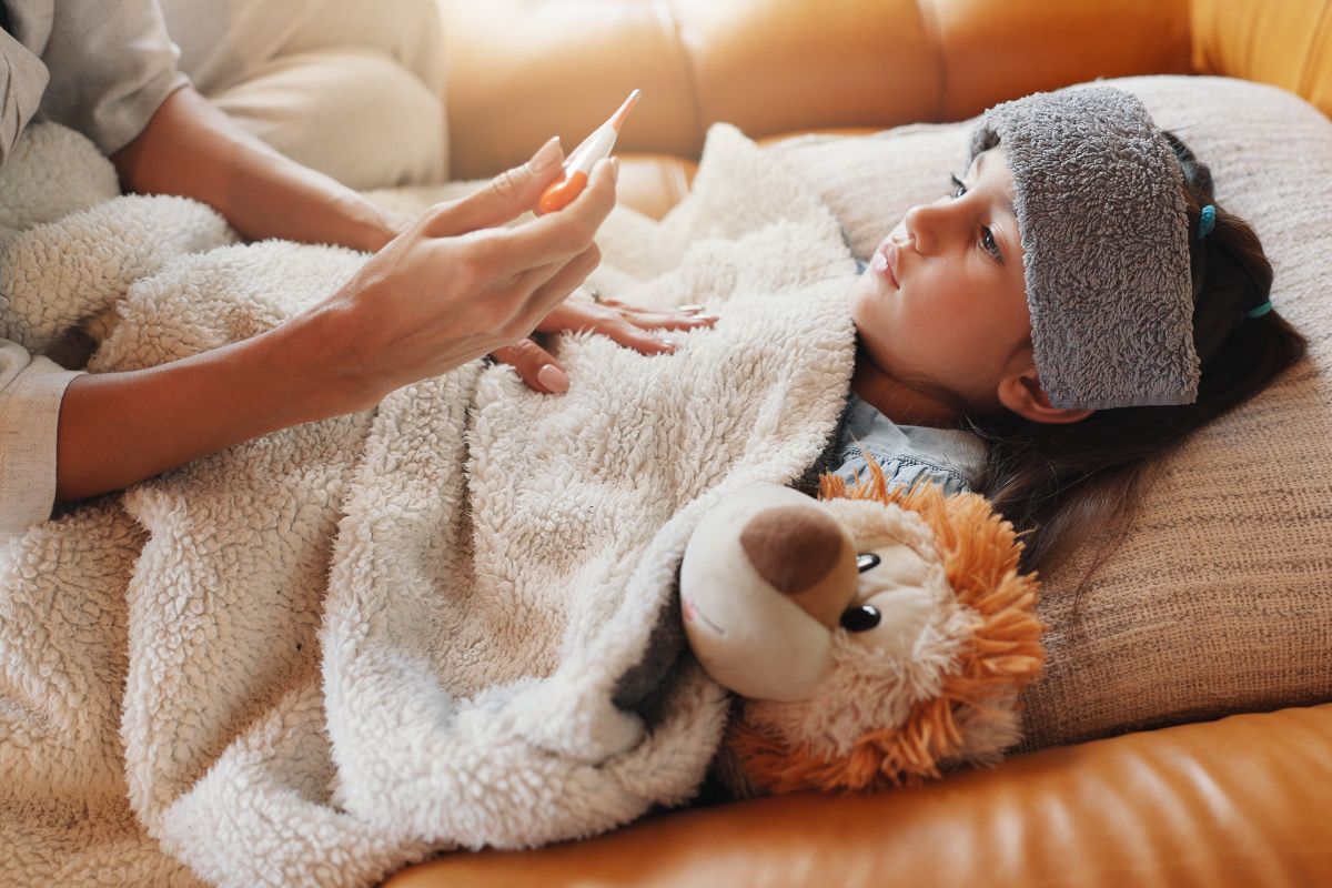 Controllo della febbre: una mamma misura la temperatura alla figlia a letto.