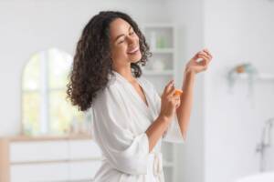 Gesto di bellezza: donna sorridente che spruzza il profumo sul proprio polso.