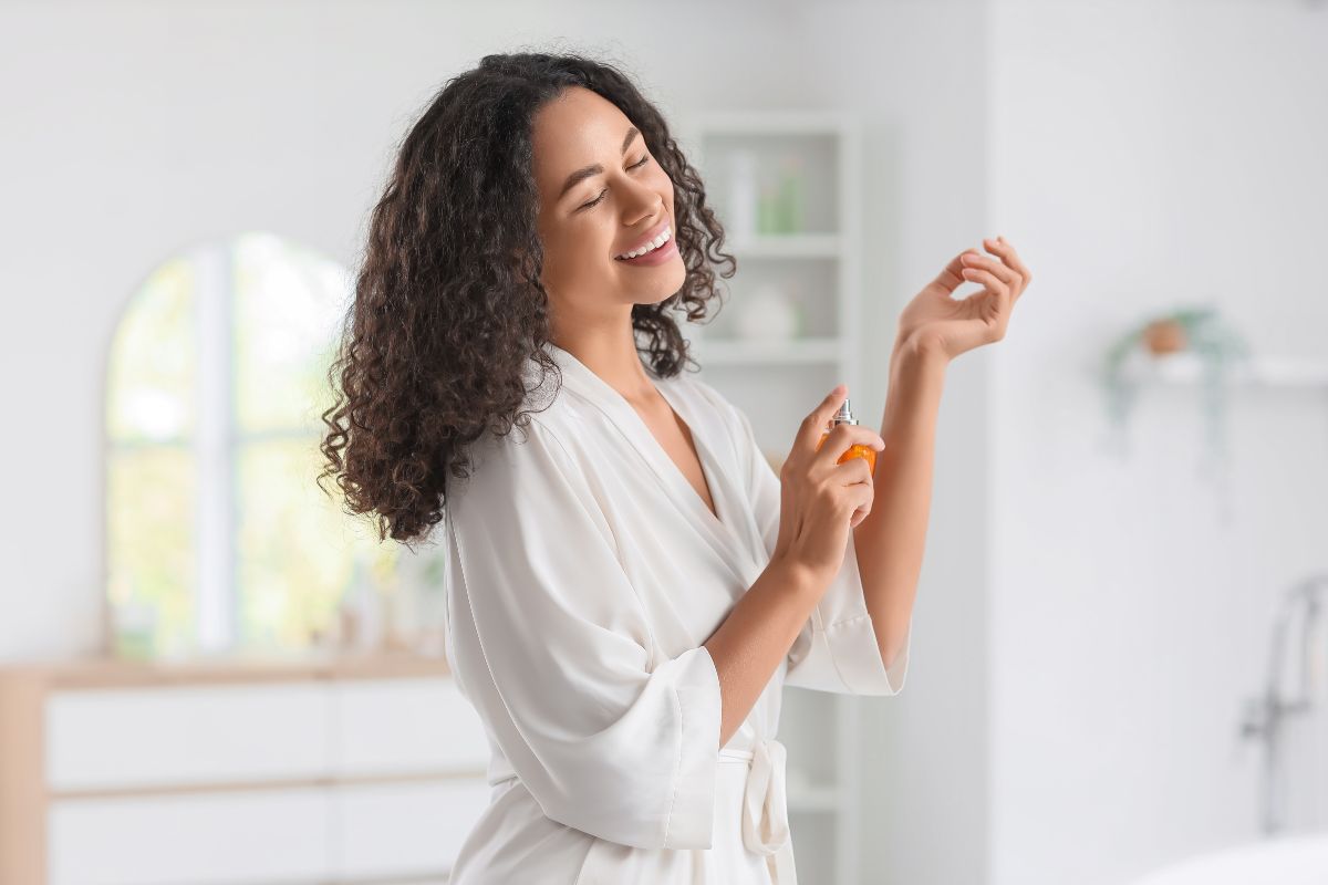 Gesto di bellezza: donna sorridente che spruzza il profumo sul proprio polso.
