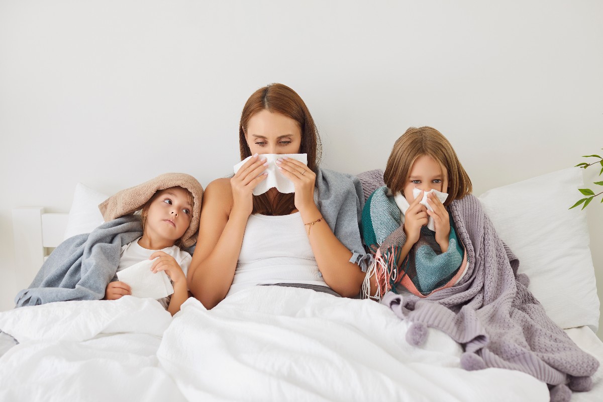 Influenza in famiglia: mamma e figlie a letto che riposano a causa del raffreddore.