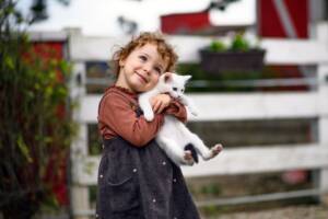 Una bambina che stringe in un abbraccio un gattino bianco.