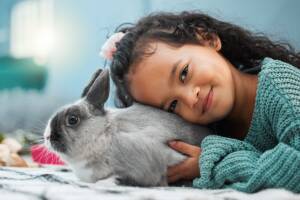 Una bambina che abbraccia teneramente il suo coniglietto grigio, inclinando il capo fino a toccare il suo dorso.