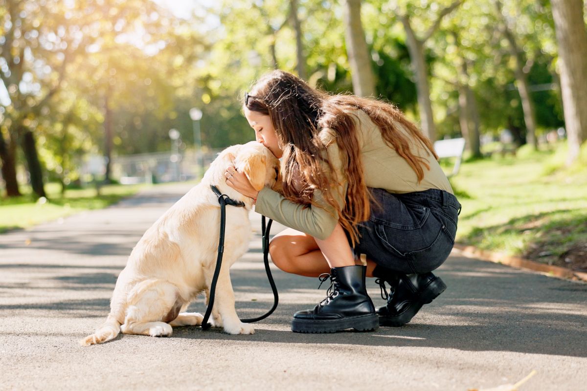 Una ragazza che si ferma durante una passeggiata per dare un bacio al suo cane.