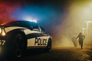Auto della Polizia ferma a bordo strada con agenti che inseguono a piedi un fuggitivo.