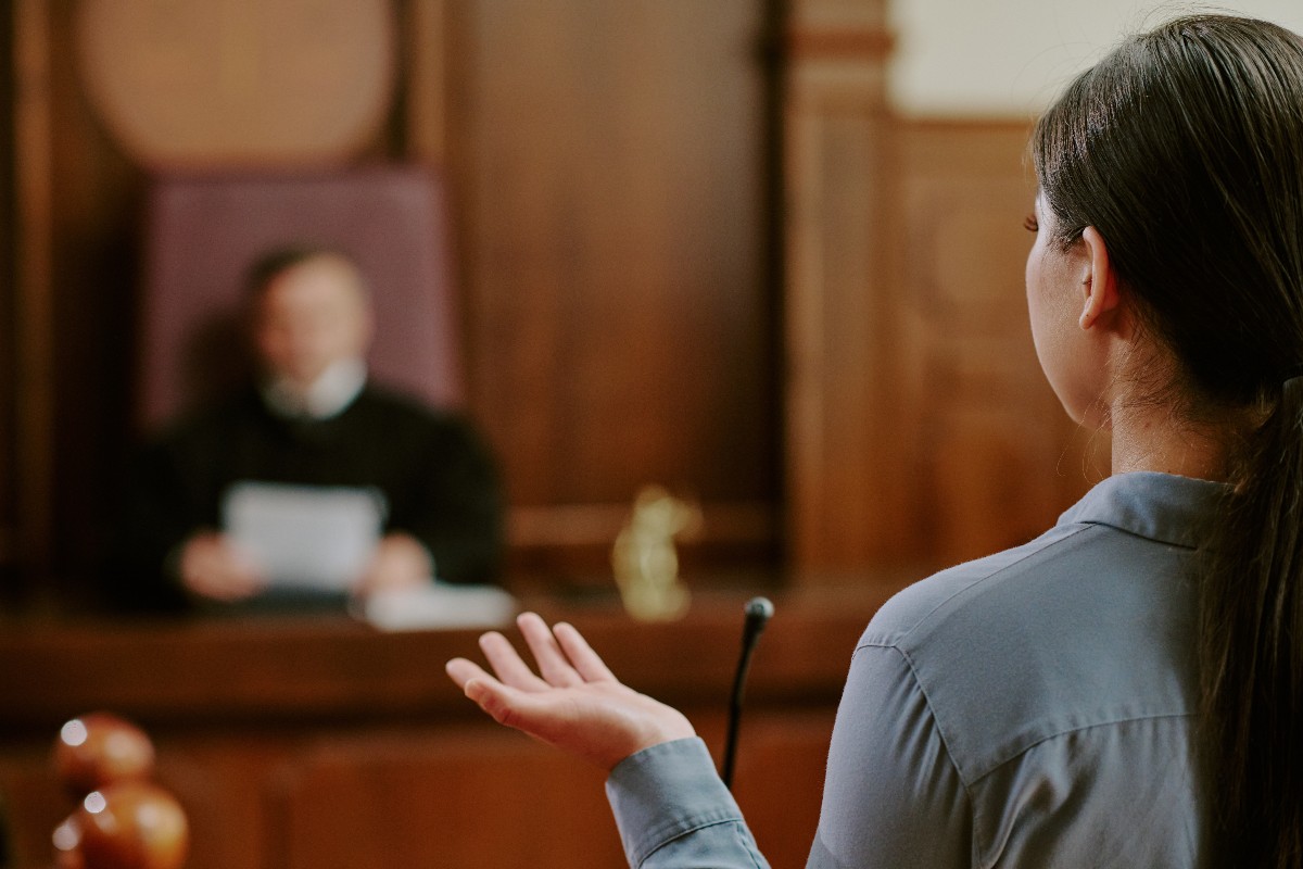 Aula di tribunale con giudice al banco e avvocato durante l'arringa.