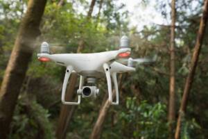 Un drone bianco in volo tra gli alberi di un bosco.