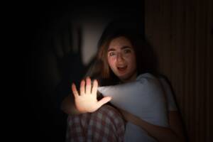 una ragazza terrorizzata che alza la mano per difendersi e abbraccia un cuscino