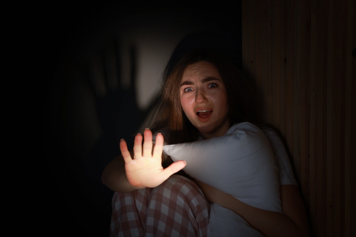 una ragazza terrorizzata che alza la mano per difendersi e abbraccia un cuscino