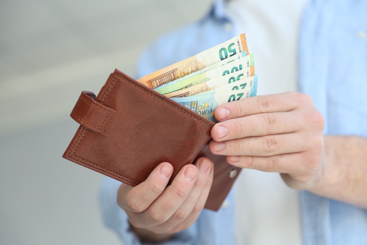 un uomo apre il portafoglio con delle banconote in euro