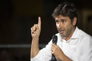 Alessandro Di Battista discute con la mano alzata e l'indice puntato verso l'alto